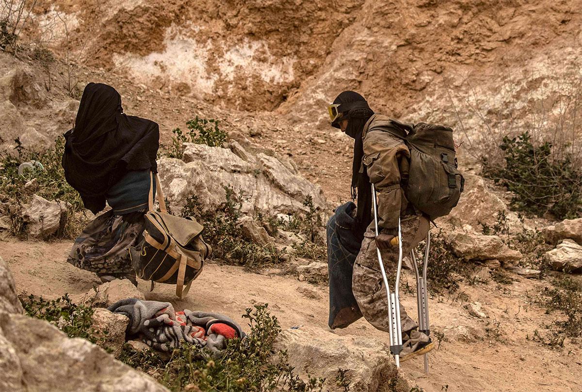 A man limps on crutches behind a woman as they walk with others said to be IS members