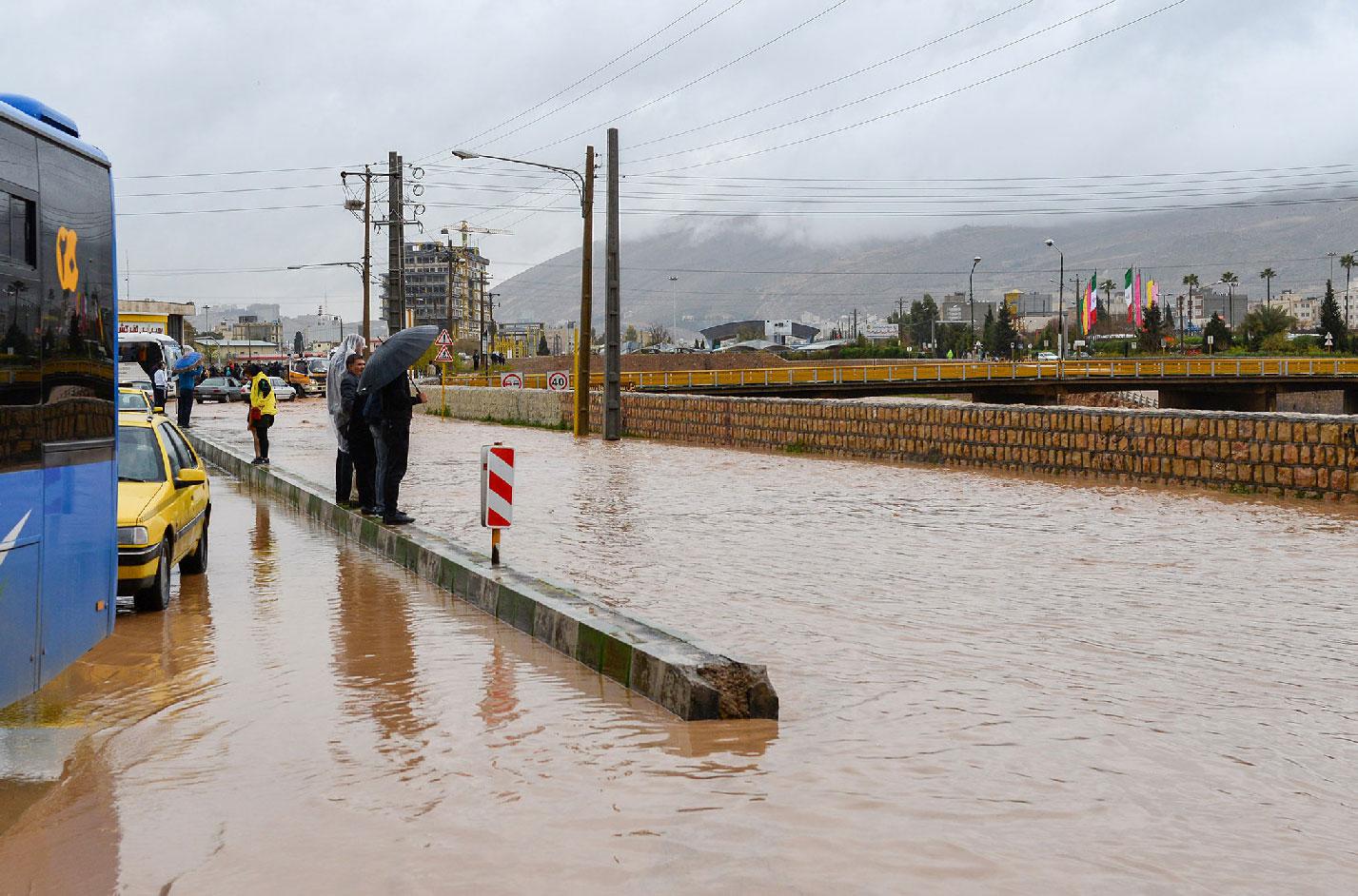 People stand near a flooded street after a flash flooding in Shiraz, Iran, March 26, 2019.