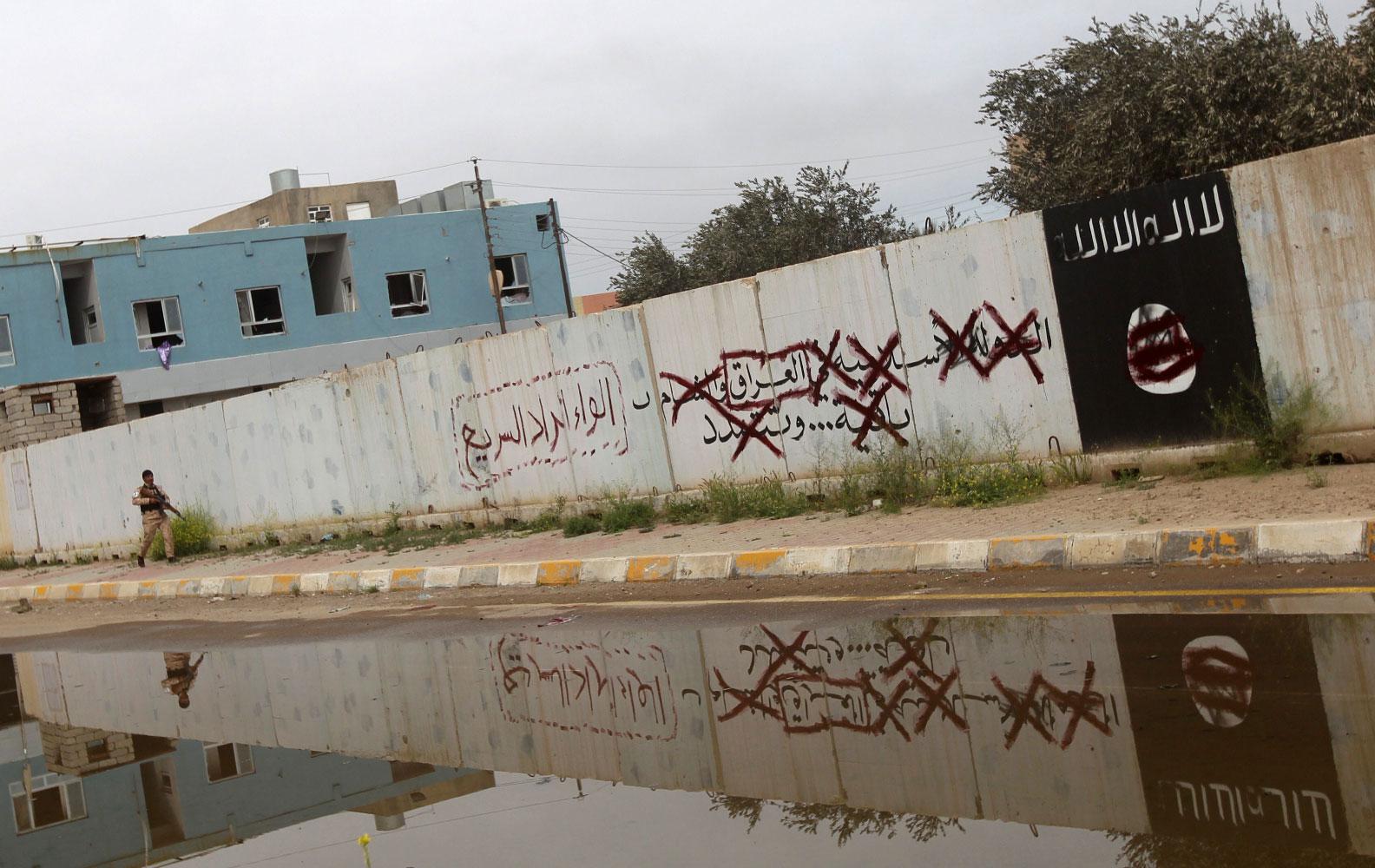 A Shiite fighter from the Popular Mobilisation units walks down an alley bearing defaced Islamist slogans and emblems in Tikrit on April 1, 2015.