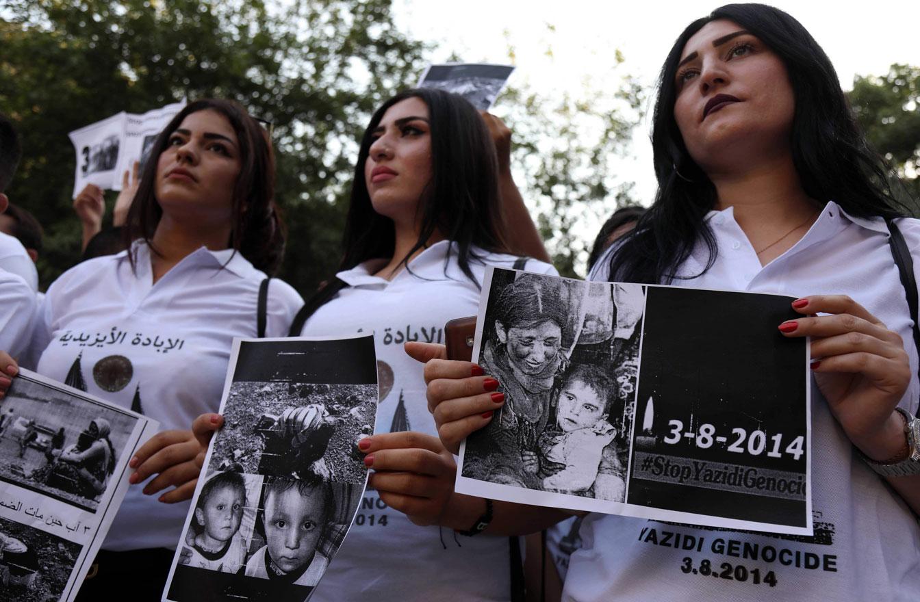 Iraqi Yazidi women hold placards with pictures of victims of the 2014 invasion of their region by the Islamic State