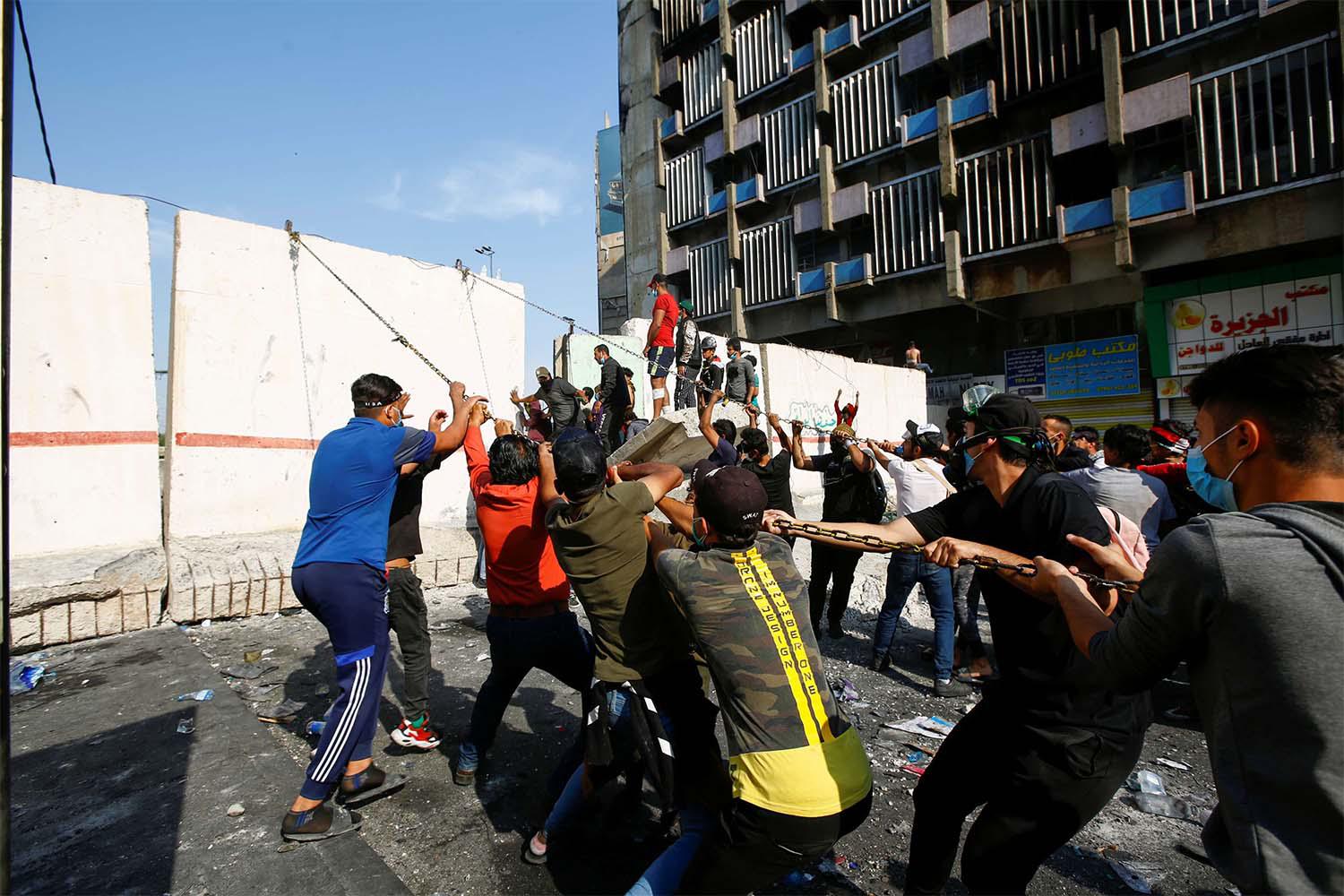 Iraqi demonstrators try to push down a concrete wall during ongoing anti-government protests in Baghdad