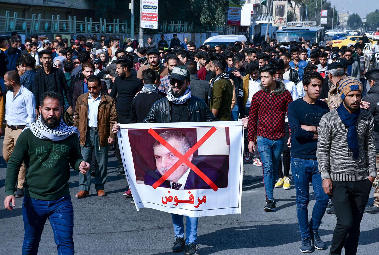 An Iraqi anti-government protester lifts a banner depicting the new Prime Minister-designate Mohammad Allawi with the inscription "rejected",