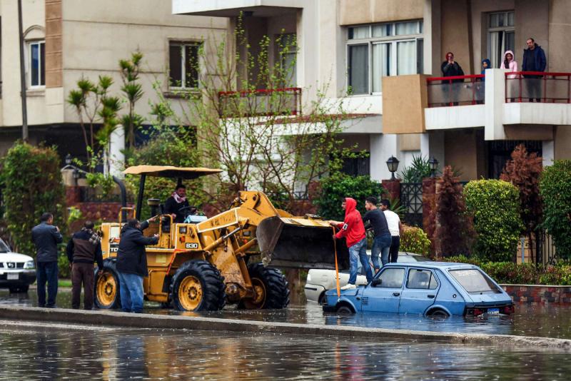 People use a bulldozer to pull out an inundated car from a flooded street in Cairo