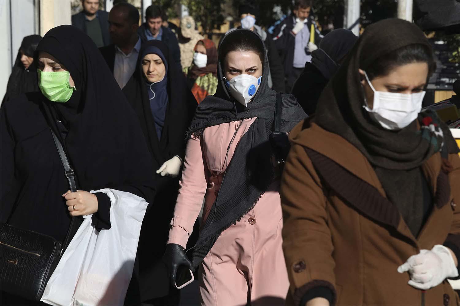 People wearing face masks walk on a sidewalk in downtown Tehran