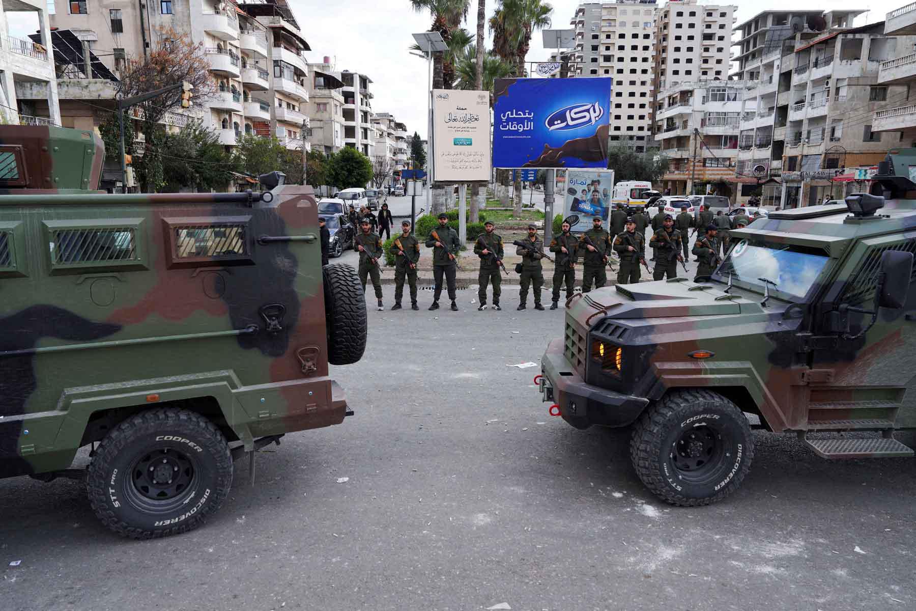 Members of the Syrian Security forces stand guard near military vehicles on the day people from the Alawite sect protest as they demand federalism, in Latakia, Syria, December 28, 2025. 