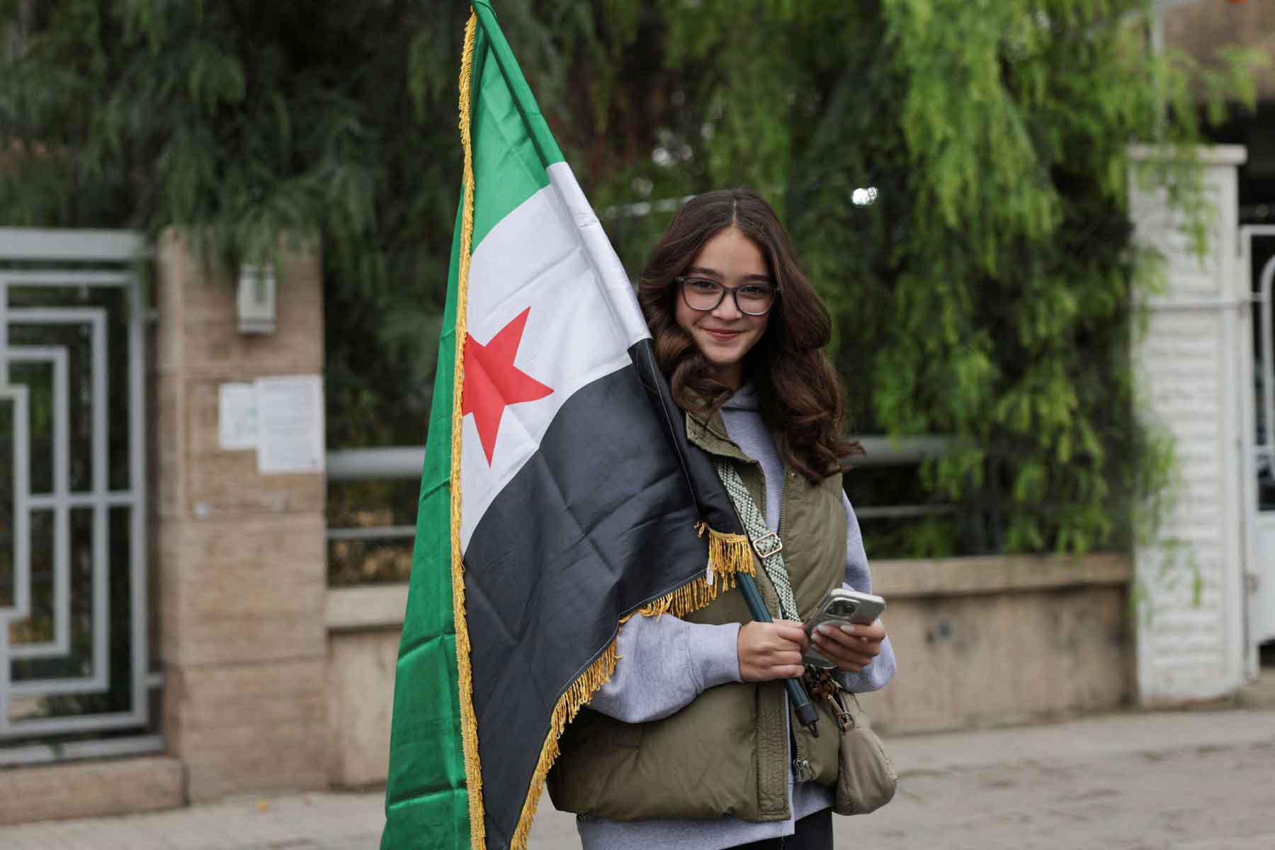 A woman holds a flag on the day of a military parade as Syrians mark the first anniversary of Bashar al-Assad’s fall, in Damascus, December 8, 2025. 